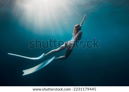 Freediver woman with white fins underwater. Freediving with beautiful girl in ocean and sun rays Royalty-Free Stock Photo #2231179445