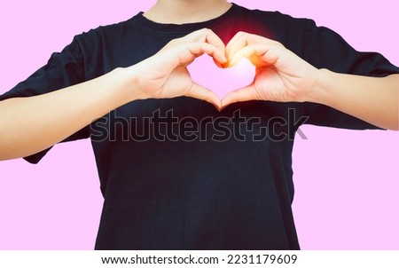 Asian girl in black shirt feeling happy and romantic, heart shape gesture showing tender feelings Poses against pink background, love and care concept of people