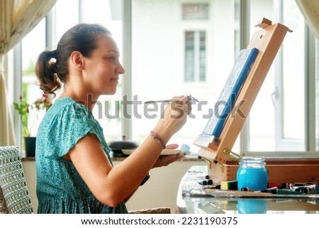 Beautiful woman painter creates pictures, drawing with paints on canvas in house. Creative hobby, activity for soul, vocation, develop skills concept