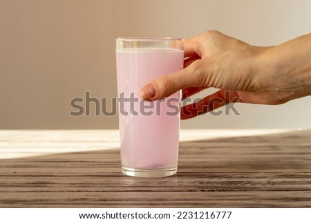 The pink electrolyte tablet dissolves in water. The woman's hand holds a glass of fizzy water with vitamin C.