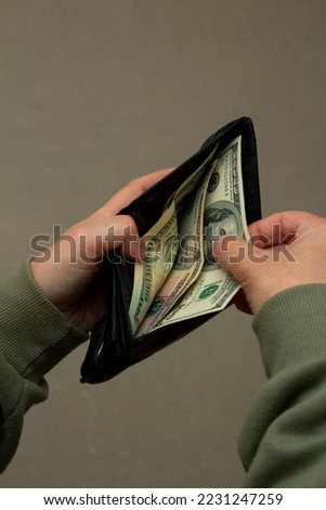Vertical photo. View from behind the shoulder. Man in a green jacket counts the money in his wallet and takes out 100 USD. One hundred dollars. View from above. Cash to pay for purchases, credit, debt