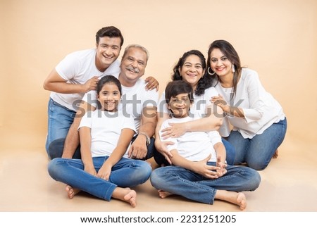 Happy indian family wearing white casual t-shirt sitting together over isolated beige background.