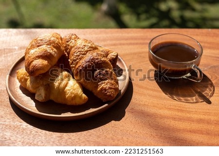 Croissant in wooden plate and cup of coffee in the morning sunshine