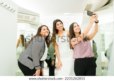 Beautiful bridesmaids taking a selfie with a young woman buying a beautiful wedding dress at the store
