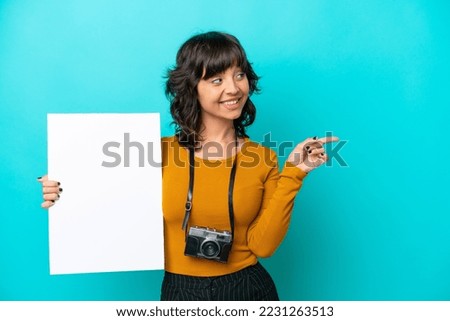 Young photographer latin woman isolated on blue background holding an empty placard and pointing side