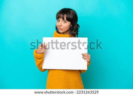 Young latin woman isolated on blue background holding an empty placard and pointing to the front