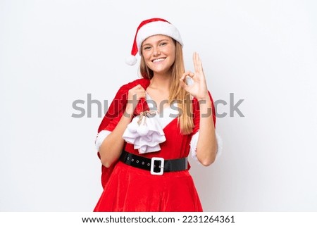 Young caucasian woman dressed as mama noel holding Christmas sack isolated on white background showing ok sign with fingers