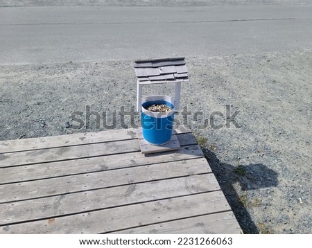 A container called a butt hut sitting on the edge of a walkway  for people to dispose of used cigarettes into it.