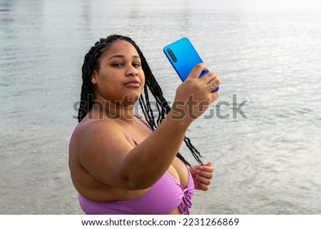 Plus size young woman uses her smartphone to take selfies. Young latin girl with braids on the beach taking pictures and smiling. body positive.