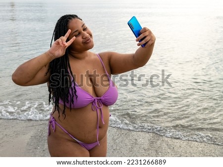 Plus size young woman uses her smartphone to take selfies. Young latin girl with braids on the beach taking pictures and smiling. body positive.