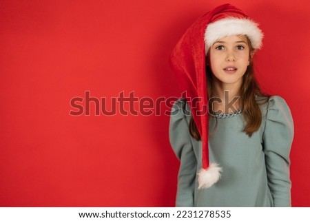 Portrait of a girl with a surprised look in the cap of a santa on a red background, the concept of Christmas, copy space.