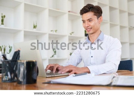 Successful young businessman using laptop at bright modern personal office.
