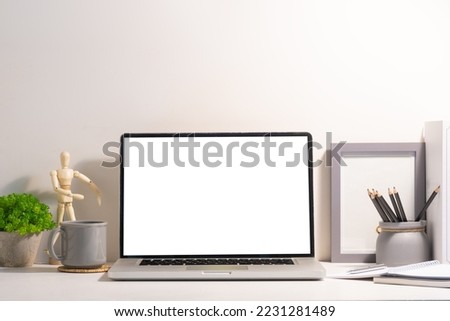 Front view of laptop computer with empty display, coffee cup and supplies on white table.