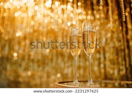 Flute glasses with bubbly wine at sparkling bokeh yellowish golden sequin garlands blaze. Bright falling gold glitter ribbons backdrop glittering twinkle decoration for celebrating luxury party Royalty-Free Stock Photo #2231297625