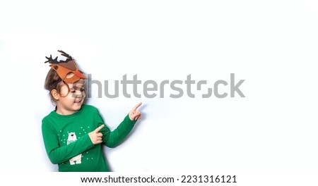 Cute caucasian kid girl in deer mask points with his finger on empty copy space for design or text. Banner. Christmas mockup template for card or certificate.
