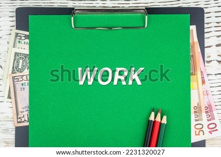WORK - word (text) euro and dollar bills on a green background, colored pencils and a wooden white table. Business concept: buying, selling, commerce (copy space).