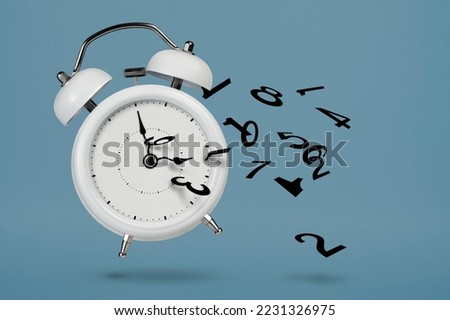 Time is running out. White alarm clock with flying numbers as a symbol of lost time. The concept of time is running out, loss or lack of time, an alarm clock with numbers shatters into small pieces. Royalty-Free Stock Photo #2231326975