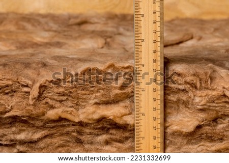 Measuring fiberglass insulation in attic of house with ruler. Home energy savings, heating and cooling costs and construction concept. Royalty-Free Stock Photo #2231332699