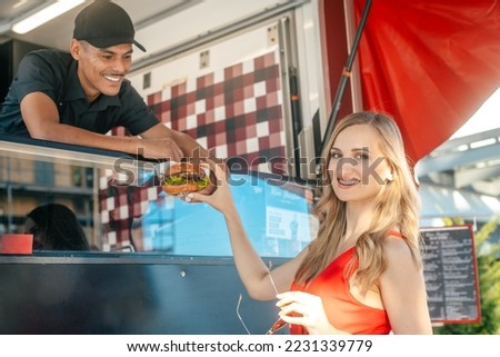 Cook in a food truck handing tasty burger over to woman customer