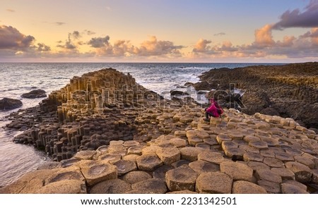 woman admiring sunset between Volcanic hexagonal basalt columns of Giant`s Causeway  in Northern Ireland Royalty-Free Stock Photo #2231342501