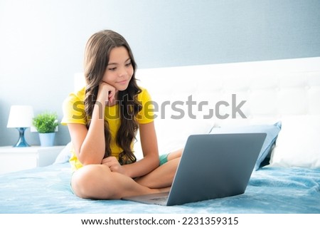 Teenager child girl browsing internet in a laptop in the bedroom at home. Happy teen girl, positive and smiling emotions.