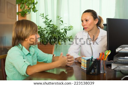 Female mature doctor examining teenage boy in office. Focus on woman 