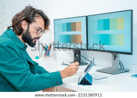 Graphic designer working with computer digital tablet stylus pen smartphone and color swatch - creative man at modern office. Architect using work tools and sample color catalog. High quality photo