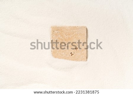 Travertine tile lying in a white sand. Top view, copy space. Minimal composition for product presentation.
