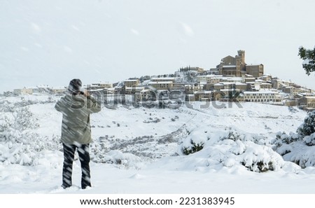 Young man taking a photo with his cell phone during a blizzard of a medieval village in an environment completely covered by snow.