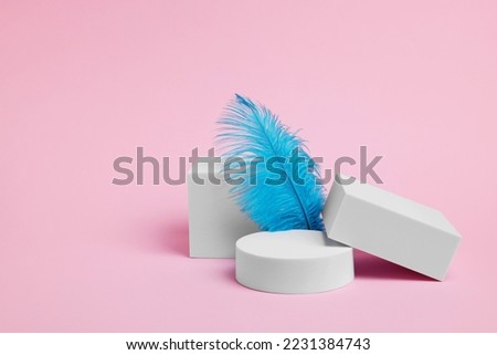 Scene for product presentation. Podiums of different geometric shapes and decorative feather on pink background, space for text