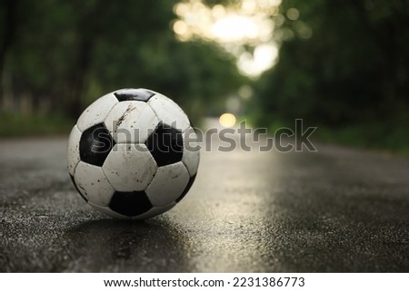 Dirty leather soccer ball on wet road, space for text