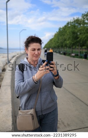 brunette woman talking on the smartphone and taking a photo with a phone in her hands. Summer sunny day in the city.
