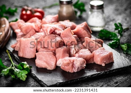 Pieces of raw pork on a stone board with parsley, tomatoes and spices. On a black background. High quality photo