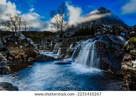 Waterfall and pool with Glen Coe in the background and blue Sky