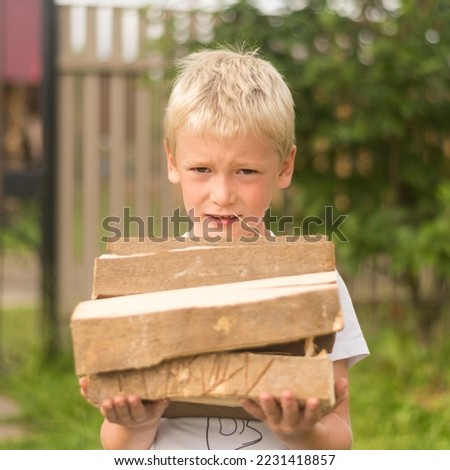 portrait of a boy with blond hair carrying an armful of firewood. the concept of preparing for winter