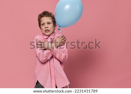 cute school age boy standing holding a blue balloon and crossing his arms over his chest