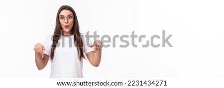 Portrait of amused and curious brunette female student inviting everyone check out very interesting event, follow this page or link, visit store, pointing fingers down, bottom advertisement. Royalty-Free Stock Photo #2231434271