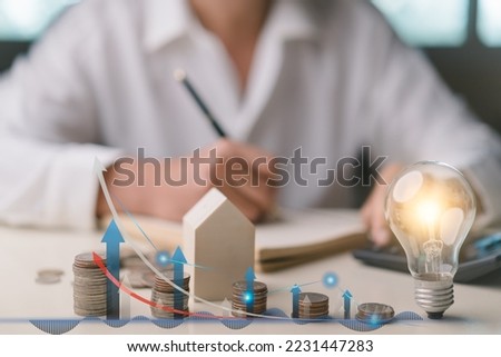 Businessman taking notes  and using calculator to calculate, Stacking coins, graph up icon, wooden house, light bulb. Plan revenue and expenses, target success growth, finance profit planning 2023.