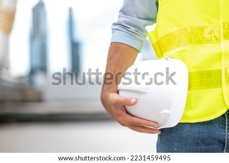 Engineer holding hardhat wearing yellow vest and standing ready for work safety in site. Royalty-Free Stock Photo #2231459495