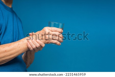 Close-up of hands senior woman trying to hold a glass of water. Causes of hand shaking include Parkinson's disease, stroke, or brain injury. Mental health neurological disorder Royalty-Free Stock Photo #2231465959