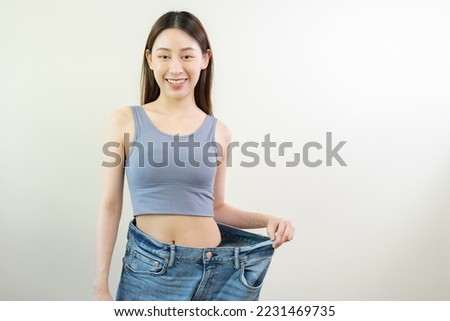Shape slender, thin waist, attractive slim asian young woman, hand show shape her weight loss, wearing in big, large or oversize jeans, excess lose by diet and exercise. People body fit healthy. Royalty-Free Stock Photo #2231469735