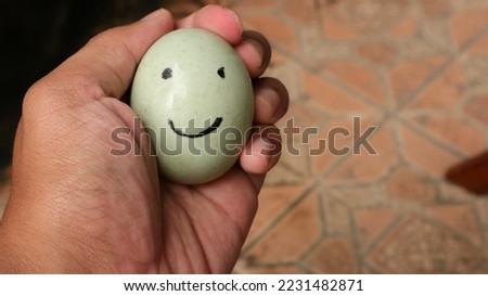 a hand holding a green egg with a smiley streak depicting someone's joy, with a blurry background, eggs are very delicious and healthy