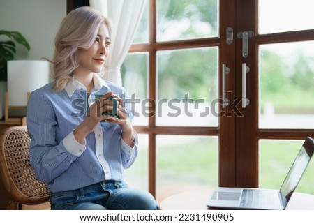 Portrait of an Asian business woman drinking coffee while working with a computer on her desk.