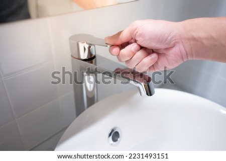 Male hand closing water tap or faucet in bathroom. Save water at home or water conservation concepts Royalty-Free Stock Photo #2231493151
