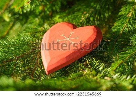 Red decorative heart with a New Year ornament on a branch of a living Christmas spruce tree in fairy tail forest. Magic atmospheric view