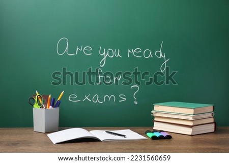 Different stationery and books on wooden table near chalkboard with phrase Are You Ready For Exams Royalty-Free Stock Photo #2231560659