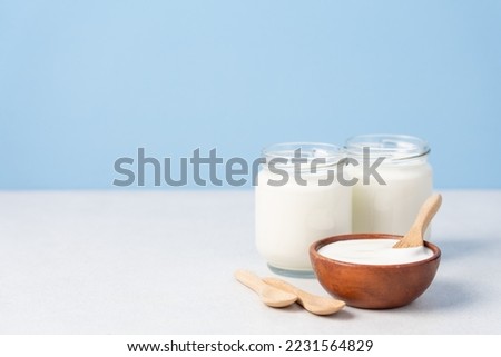 Wooden bowl and glass jars with yogurt on blue background. Healthy breakfast from milk or alternatives on light table side view