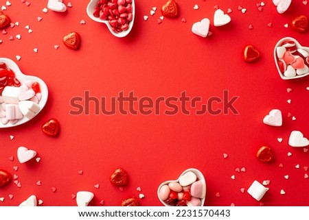 Valentine's Day concept. Top view photo of heart shaped saucers with confectionery chocolate jelly candies and confetti on isolated red background with empty space in the middle