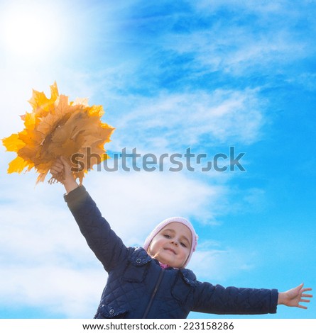 Happy Little Girl with bouquet autumn yellow dry leaves on blue sky