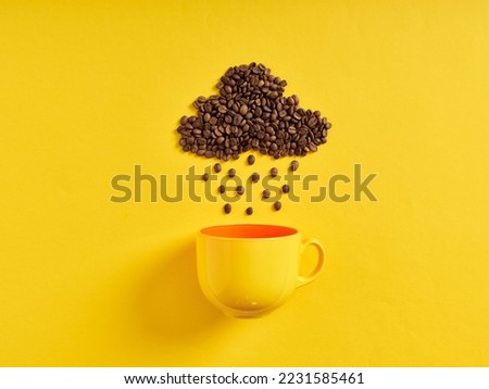 Raining coffee concept. Coffee beans in shape of rain cloud and raindrops raining towards the coffee cup on yellow background.